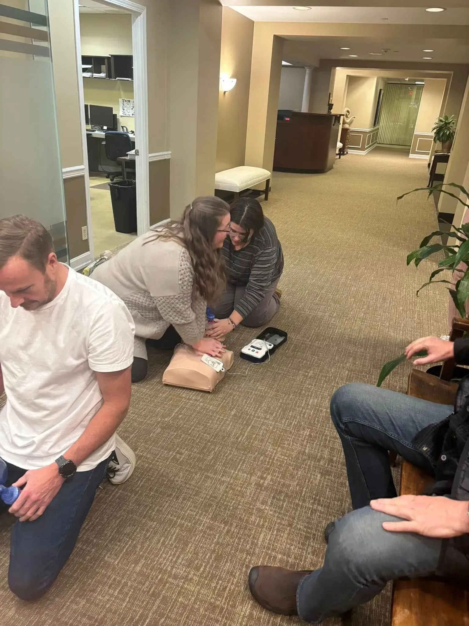 People practicing CPR on a training dummy in a hallway.