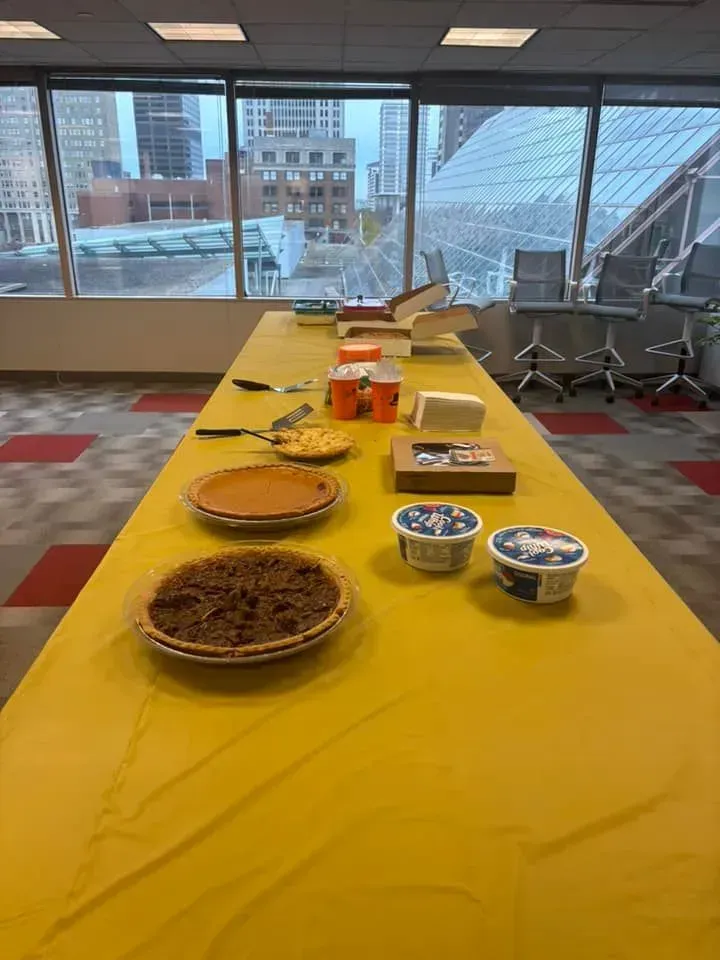 A long table covered in yellow with pies, snacks, and whipped cream, by a window.