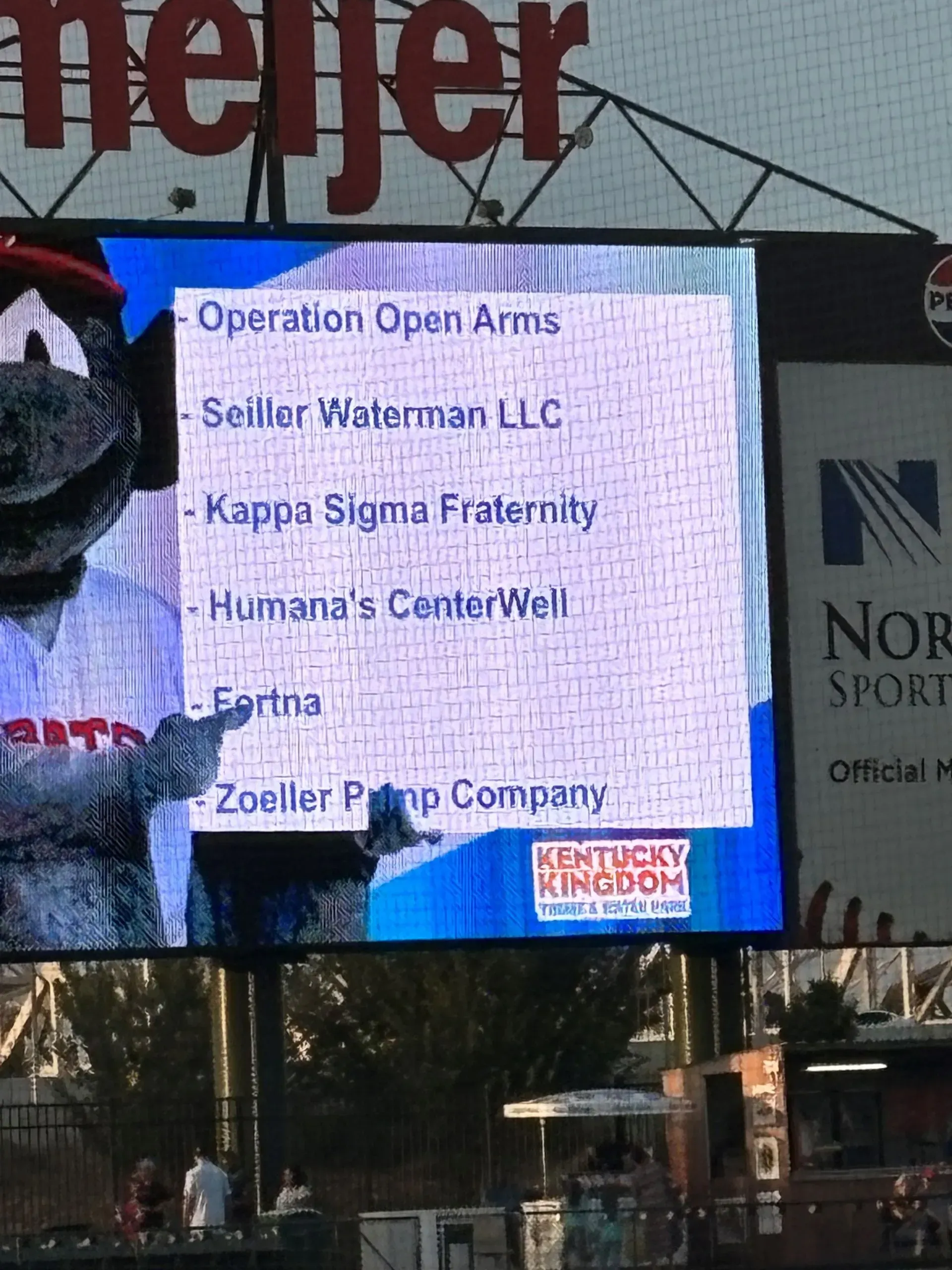 List of sponsors on a stadium screen: Operation Open Arms, Kappa Sigma, and Zoeller Pump, with a mascot.