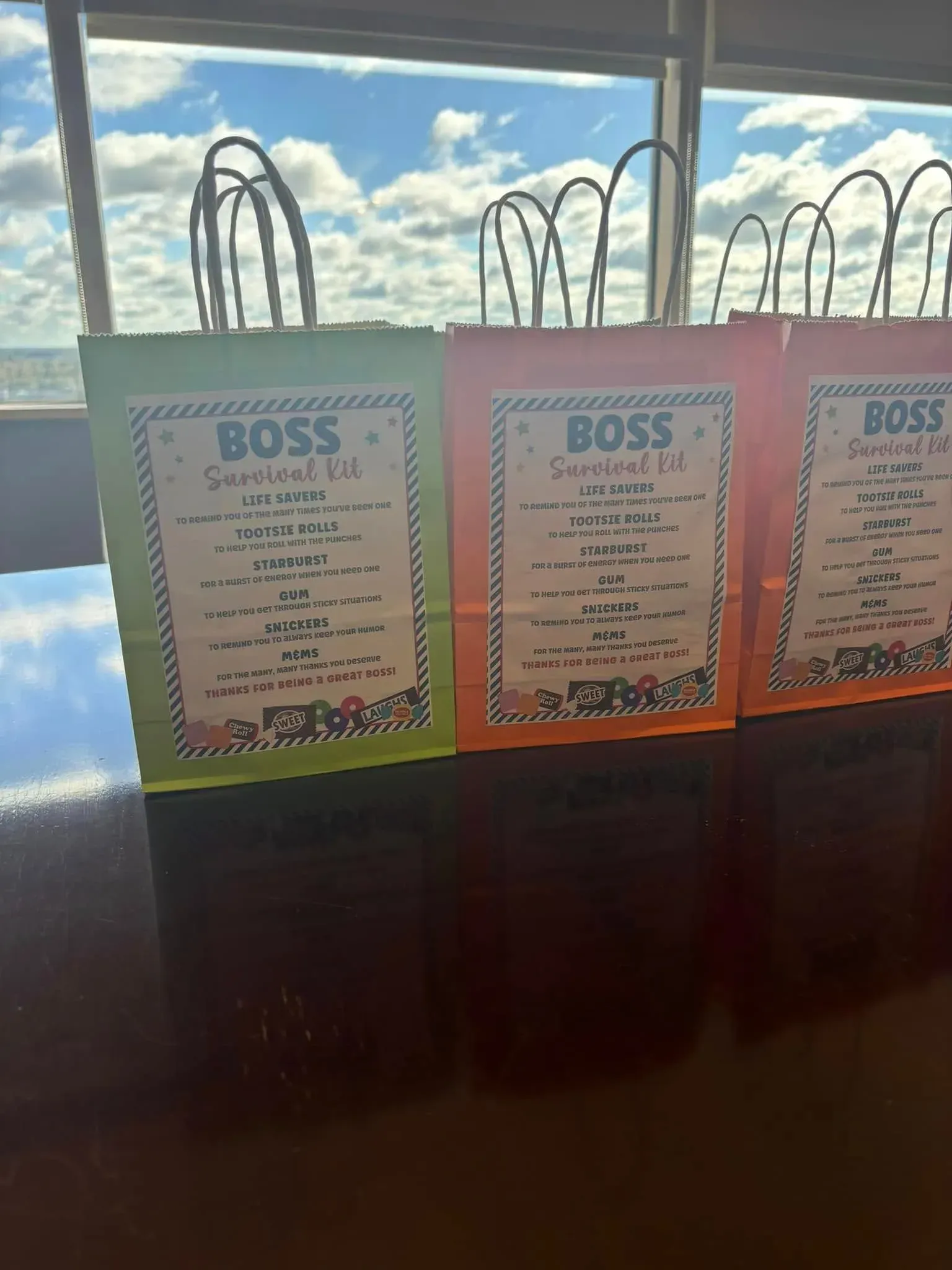 Three colorful gift bags with labels, set against a window and sky background.