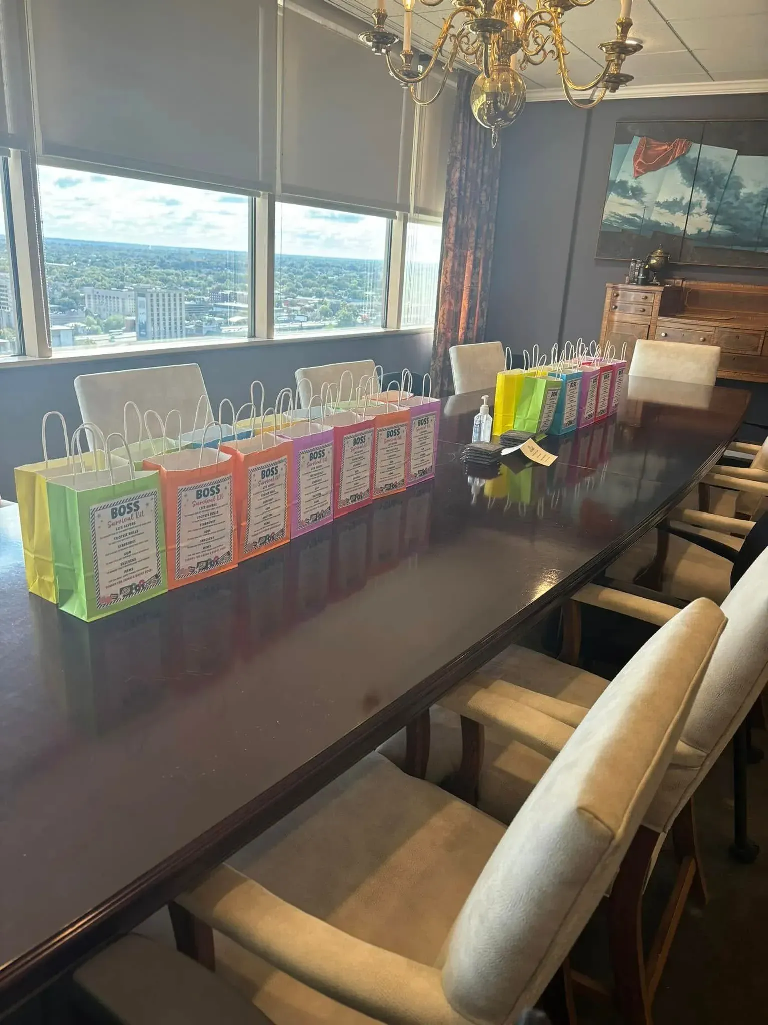 Long conference table with colorful gift bags set out for an event with city view.