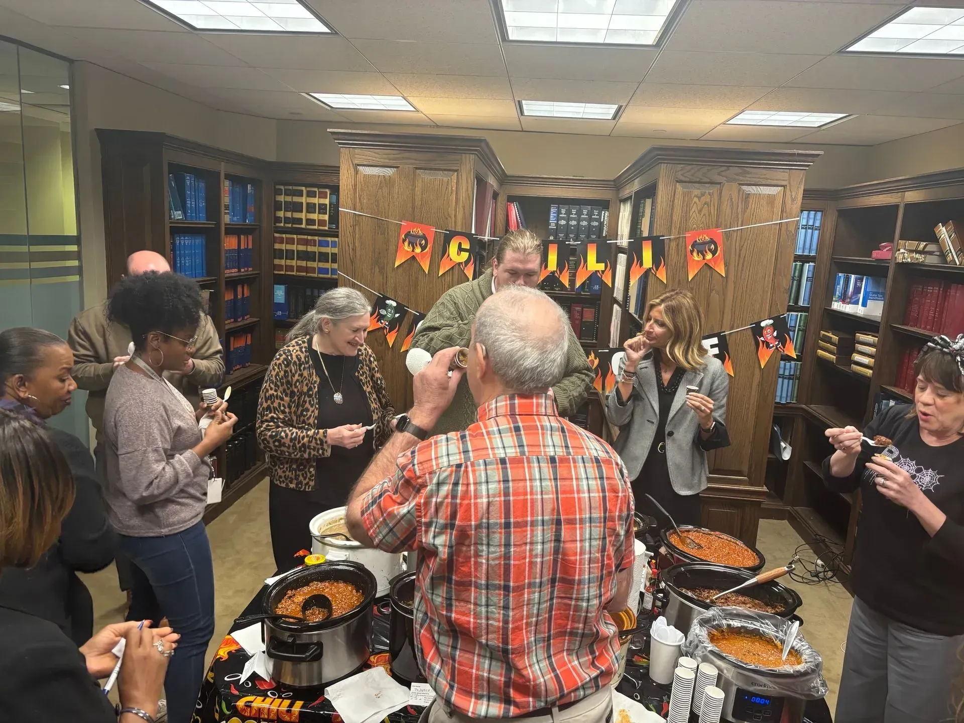 People at a Halloween chili cook-off in a library with decorations and chili pots.