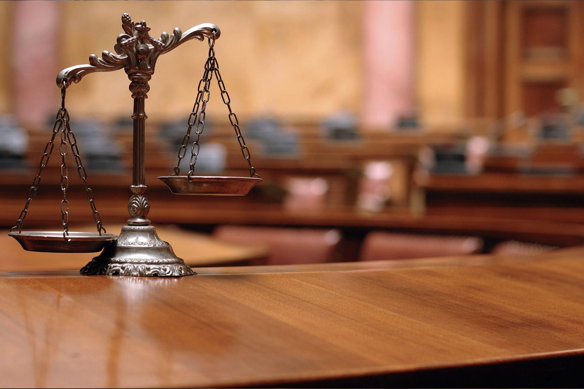 Scale of justice on a wooden table in a courtroom.