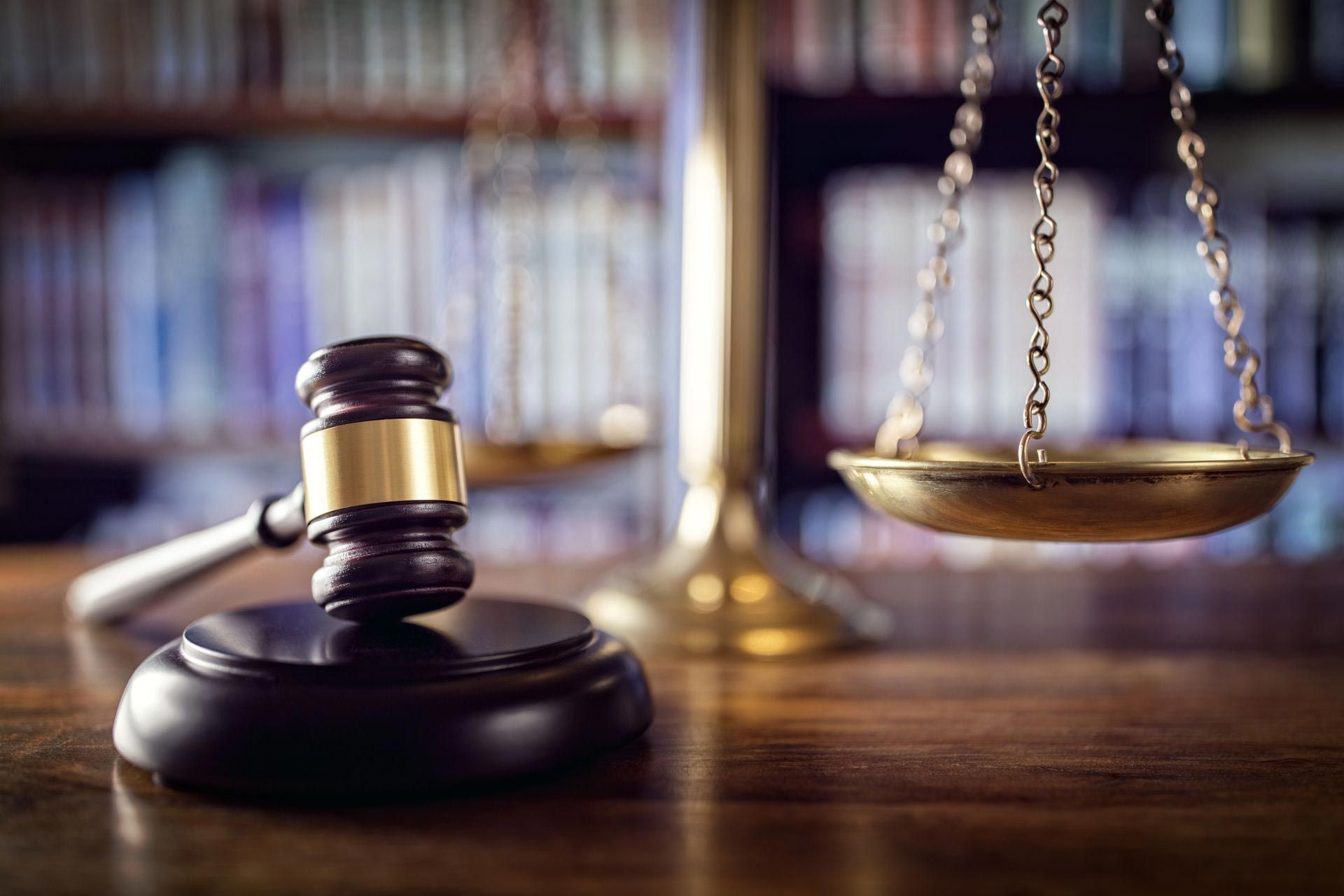 Gavel and scales of justice on a wooden desk in front of a bookshelf.