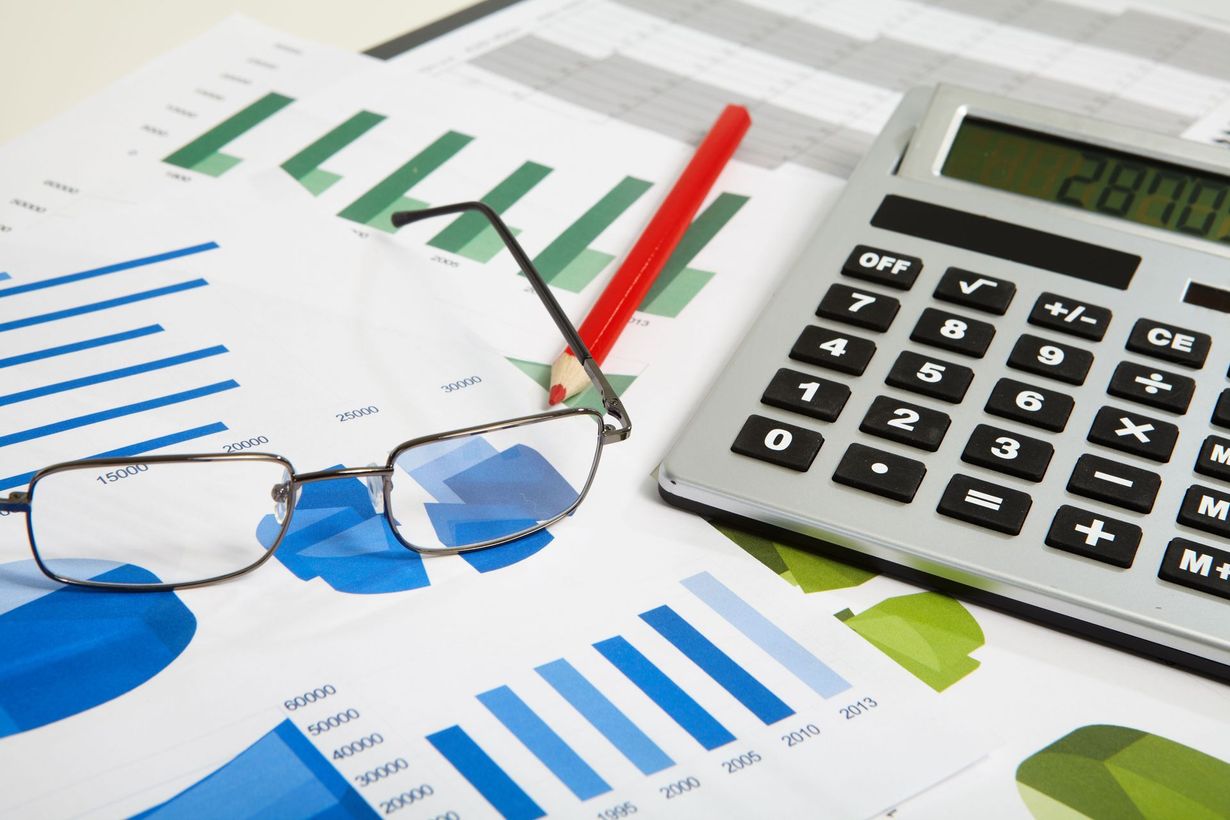 Graphs, calculator displaying 2870, glasses, and red pencil on financial documents.