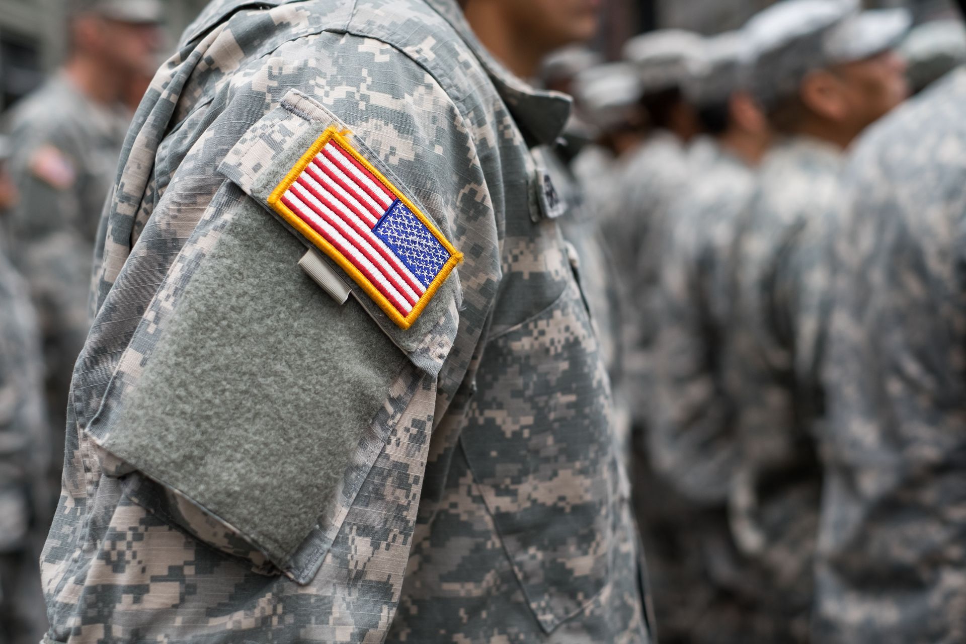 Soldier in camouflage uniform with US flag patch, standing in formation.