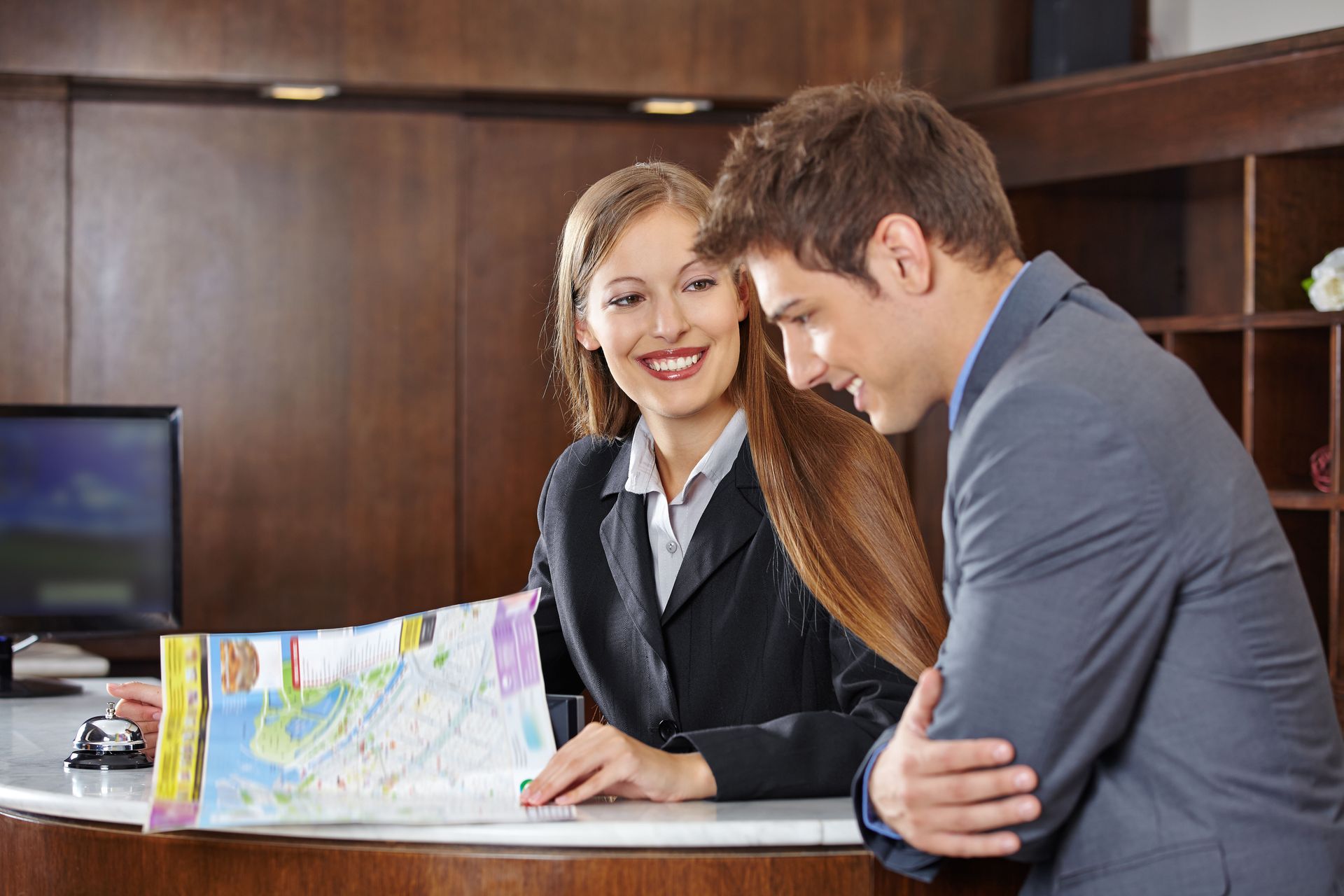 Hotel receptionist assisting a guest with a map. They are smiling at each other by a desk.
