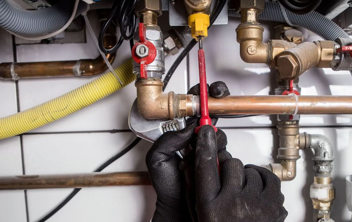 A person with gloved hands is using tools on copper pipes near a furnace.