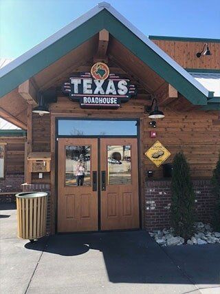The front of a texas roadhouse restaurant with wooden doors and a trash can.