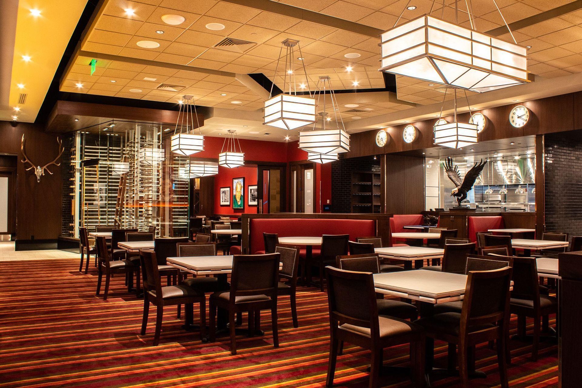 Empty upscale restaurant interior with red booths, wooden tables, and hanging square lights