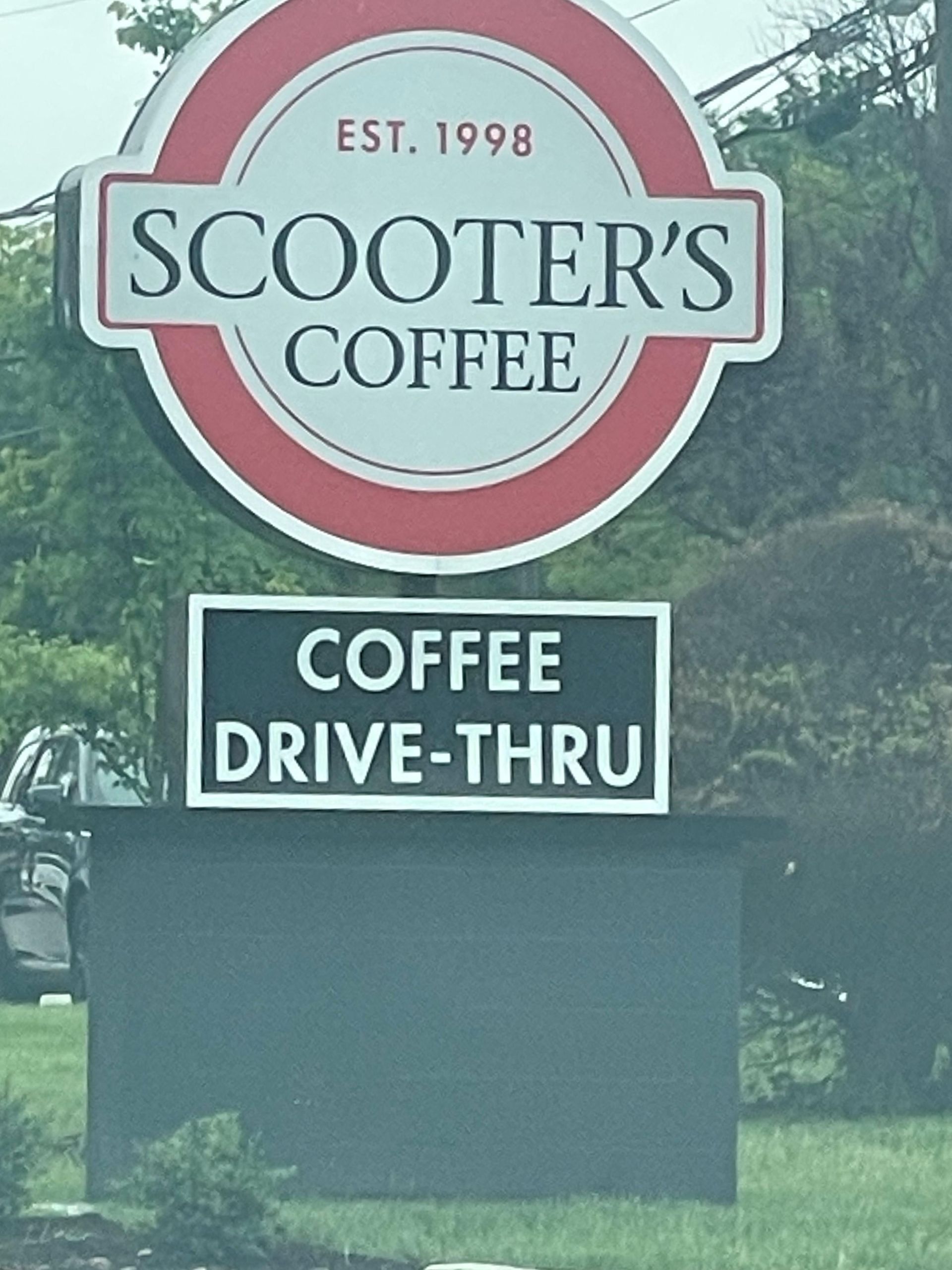 Scooter’s Coffee sign with “Coffee Drive-Thru” on a black roadside board.