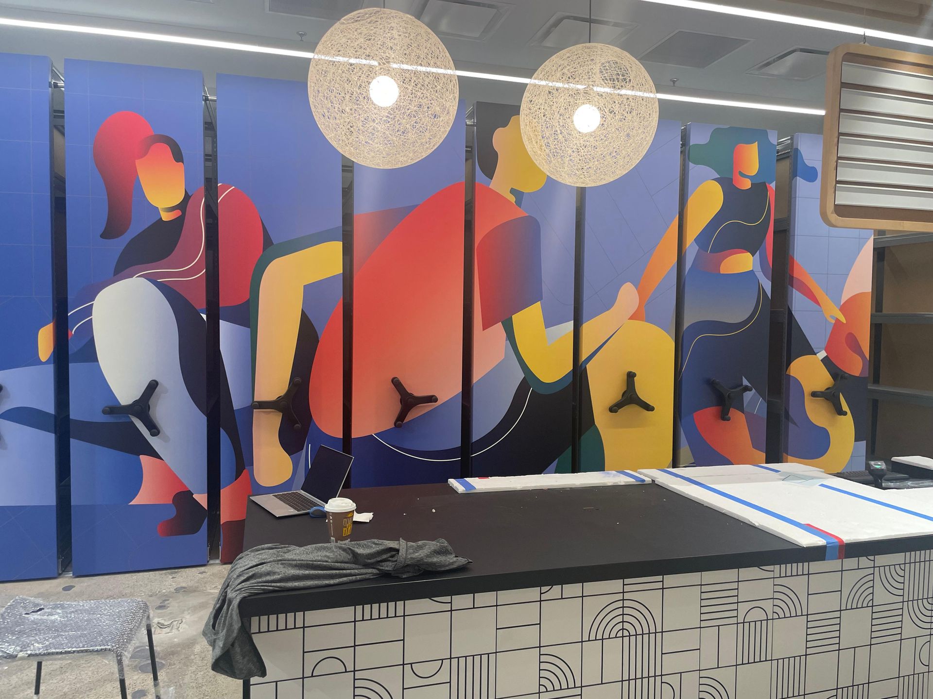 Colorful abstract mural on a wall with hanging round lights and a patterned bench in front