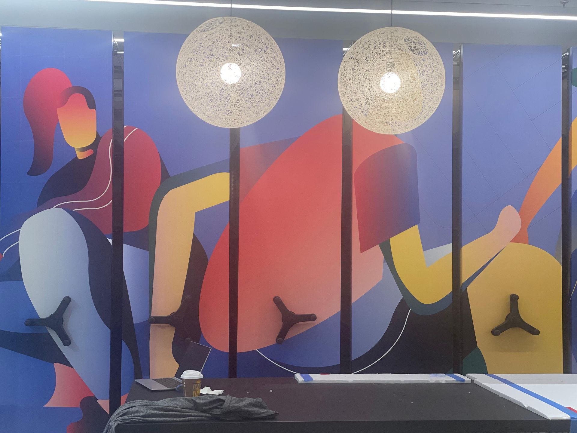Colorful abstract mural of two musicians playing guitars behind two hanging woven lamps.