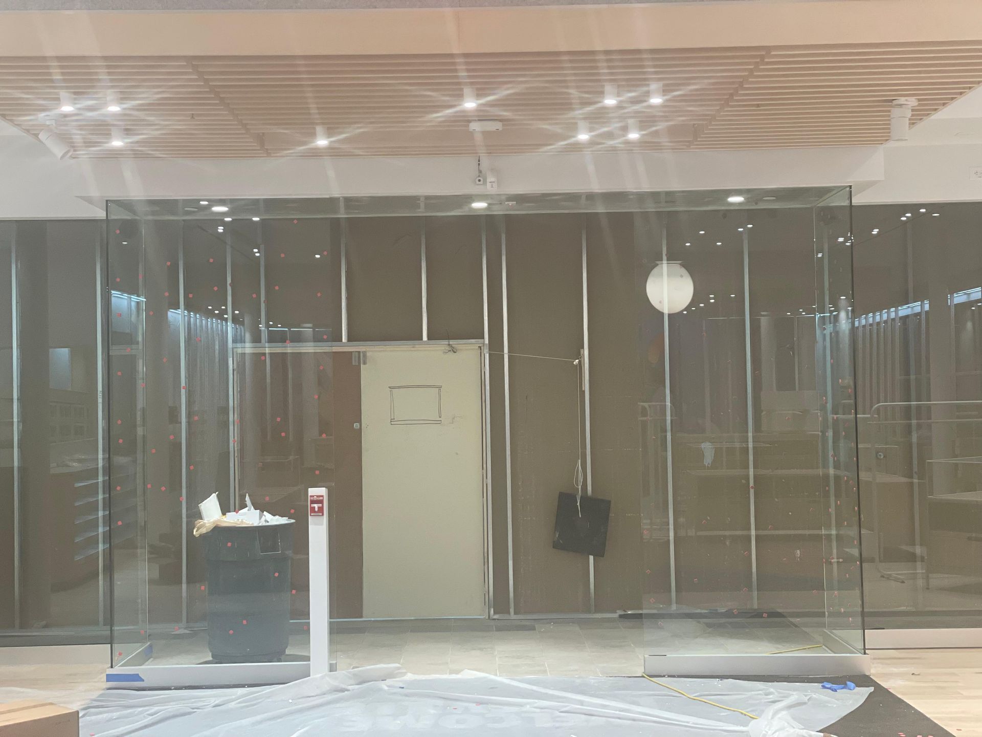Empty storefront with clear plastic strip curtains, glass doors, and ceiling lights inside a mall.