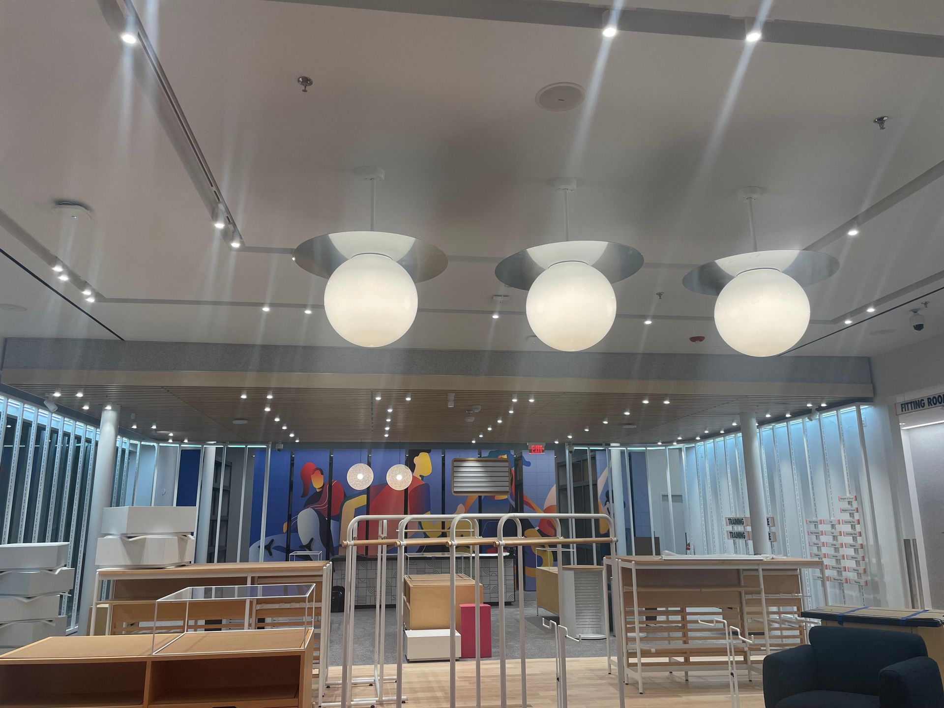 Modern dining hall with round hanging lights, long tables, and a colorful mural at the back.