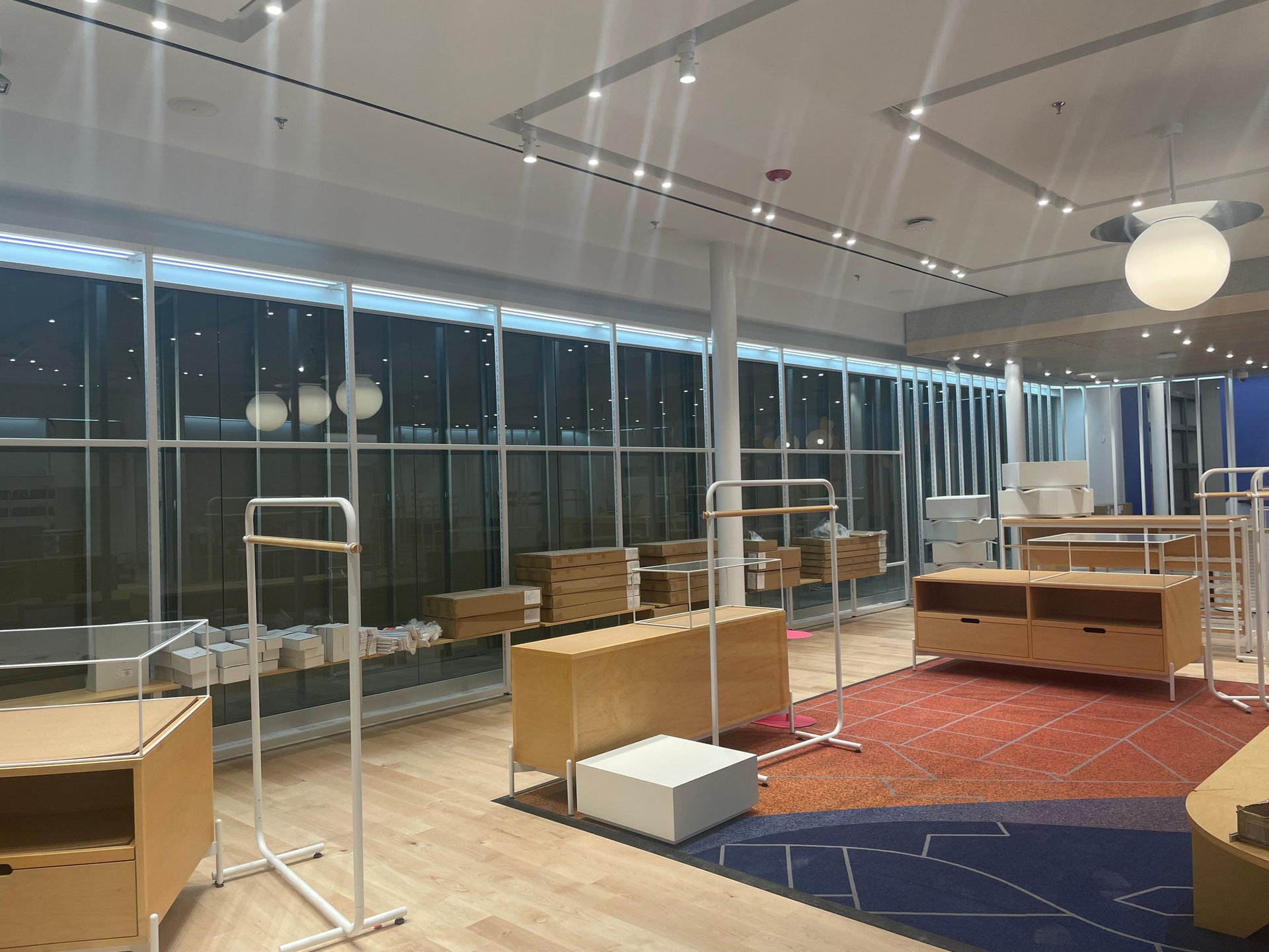 Empty retail store interior with display fixtures, boxes, and a red rug under bright lights.