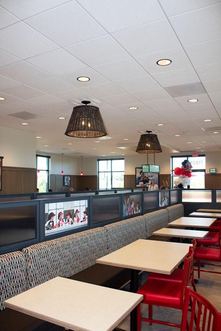 Empty restaurant dining area with red chairs, white tables, and hanging pendant lights
