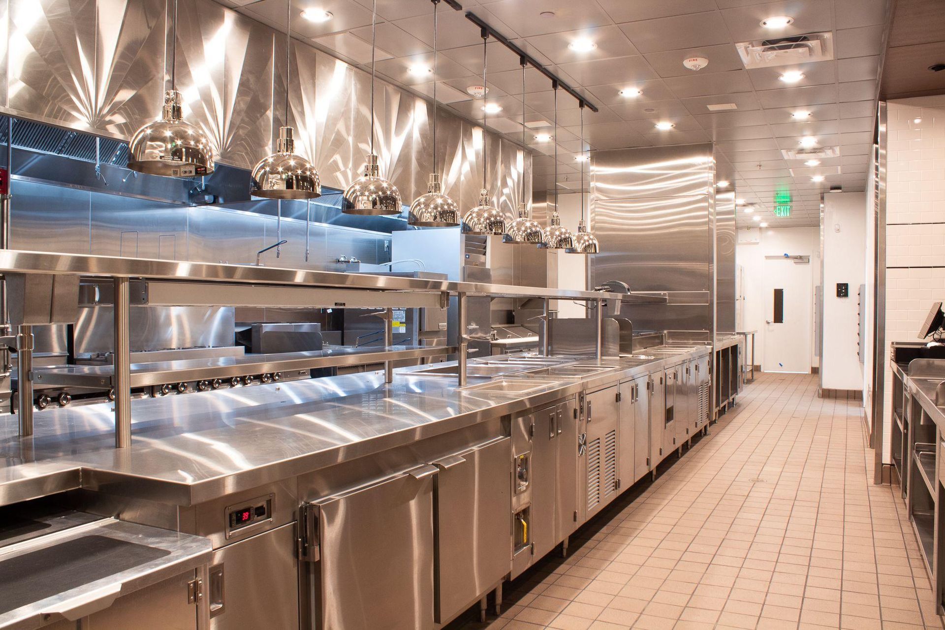 Modern commercial kitchen with stainless steel counters, hanging pots, and bright overhead lighting