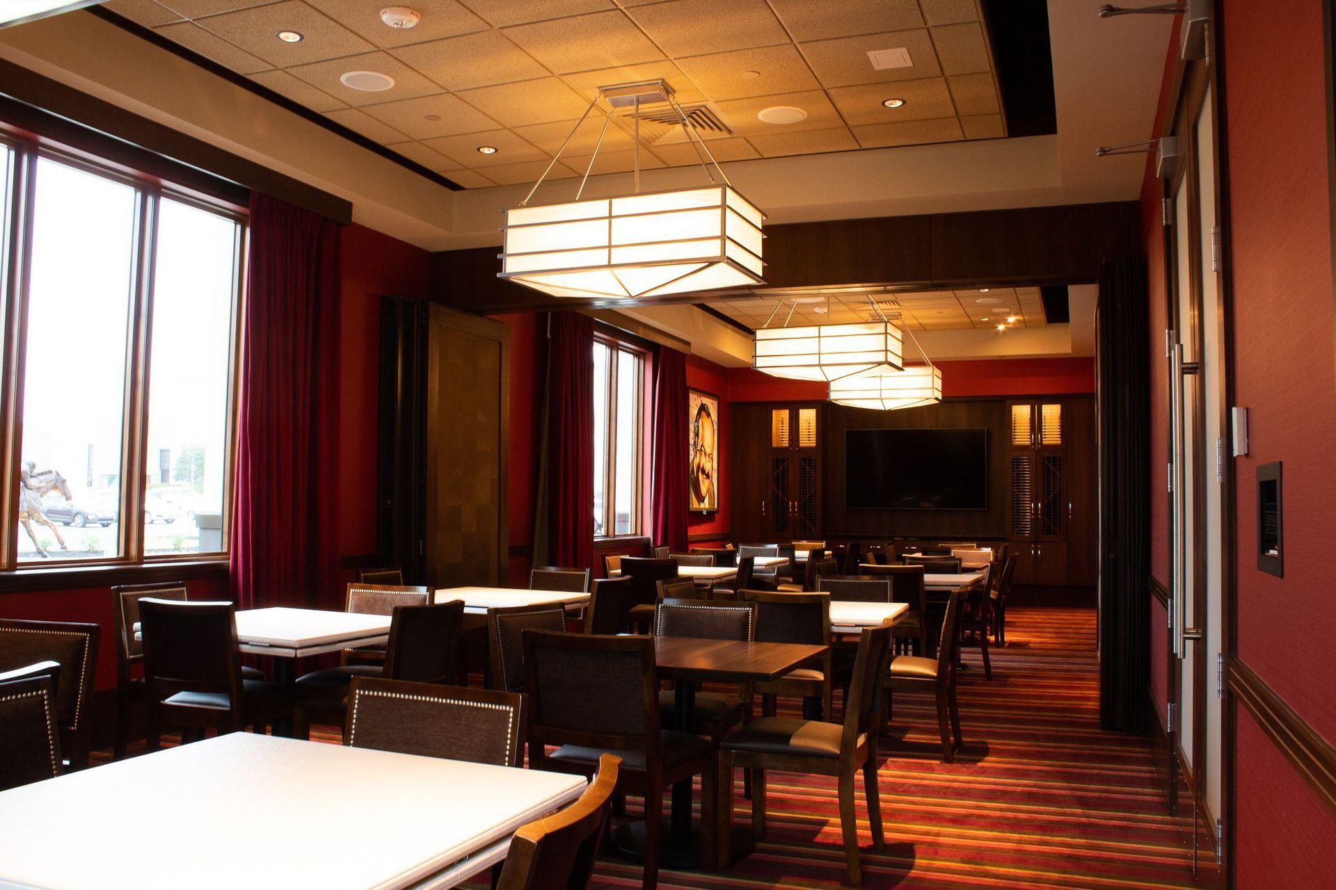 Empty restaurant dining room with tables, chairs, red curtains, and warm ceiling lights
