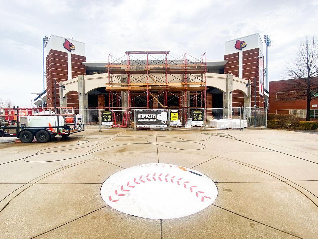 Construction site with scaffolded stadium entrance and a baseball logo on the pavement