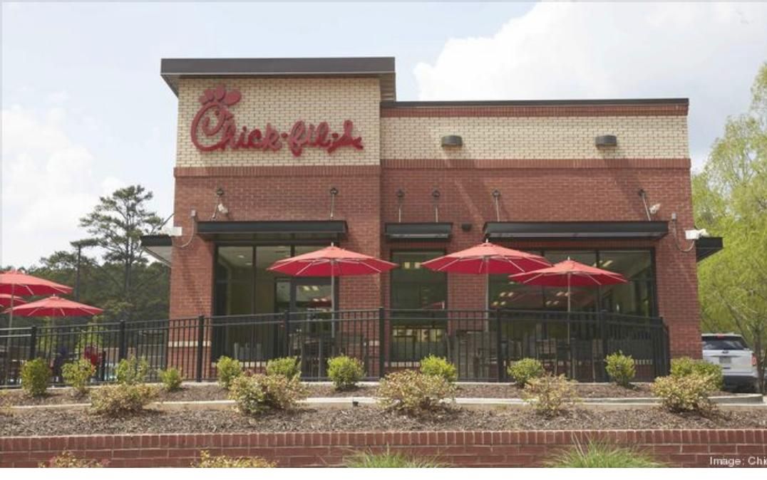 Chick-fil-A restaurant exterior with red umbrellas and outdoor seating behind a black fence