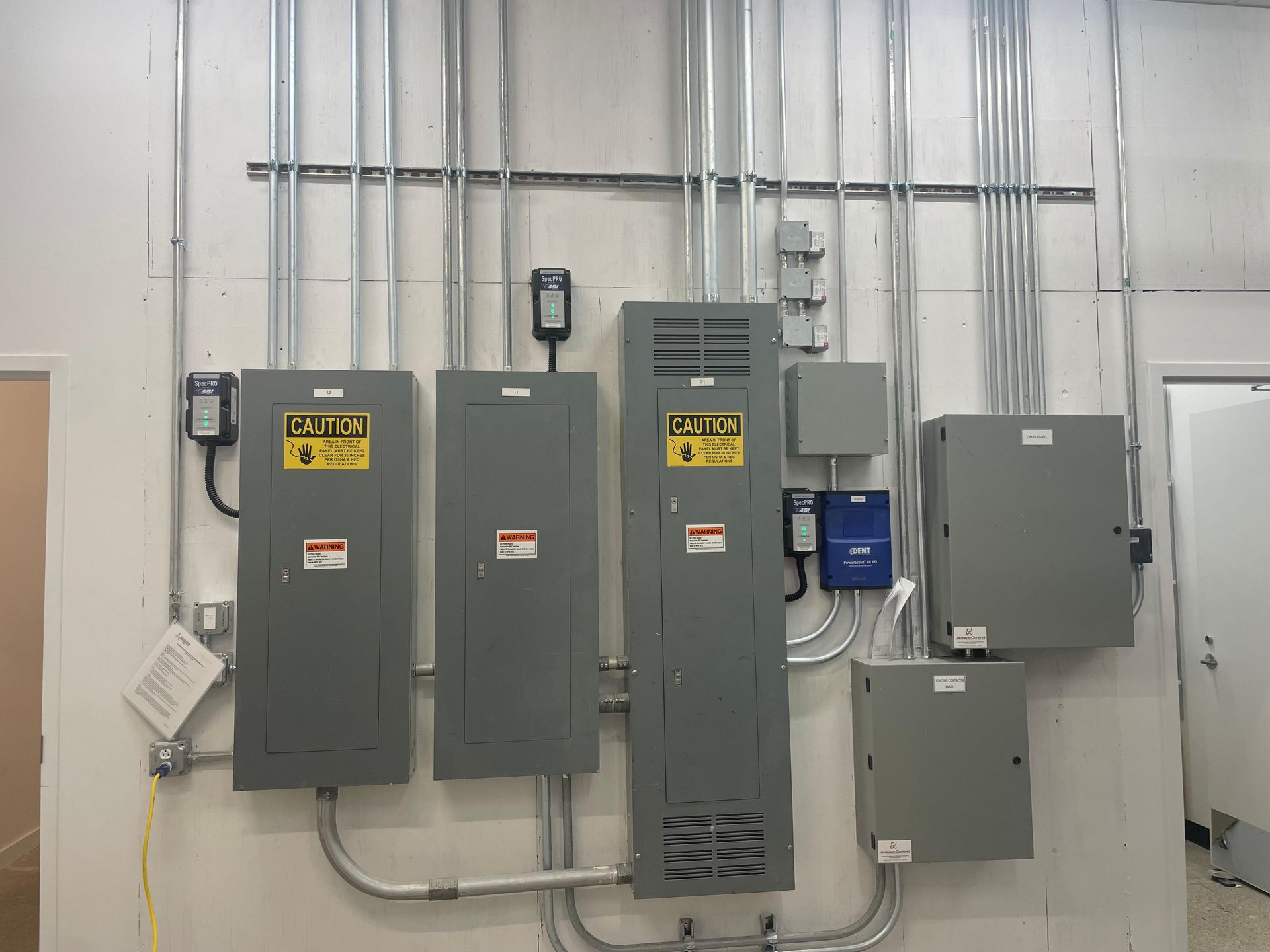 Electrical panels and conduit mounted on a metal wall in an industrial utility room.