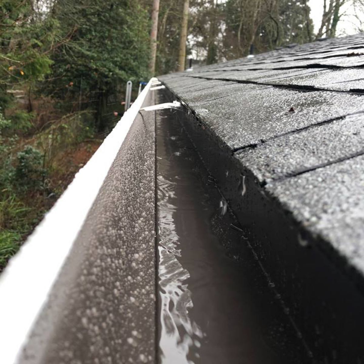 A close up of a gutter on a roof with water coming out of it.