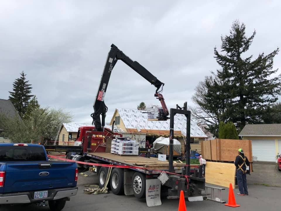 A truck with a crane on top of it is parked in front of a house under construction.