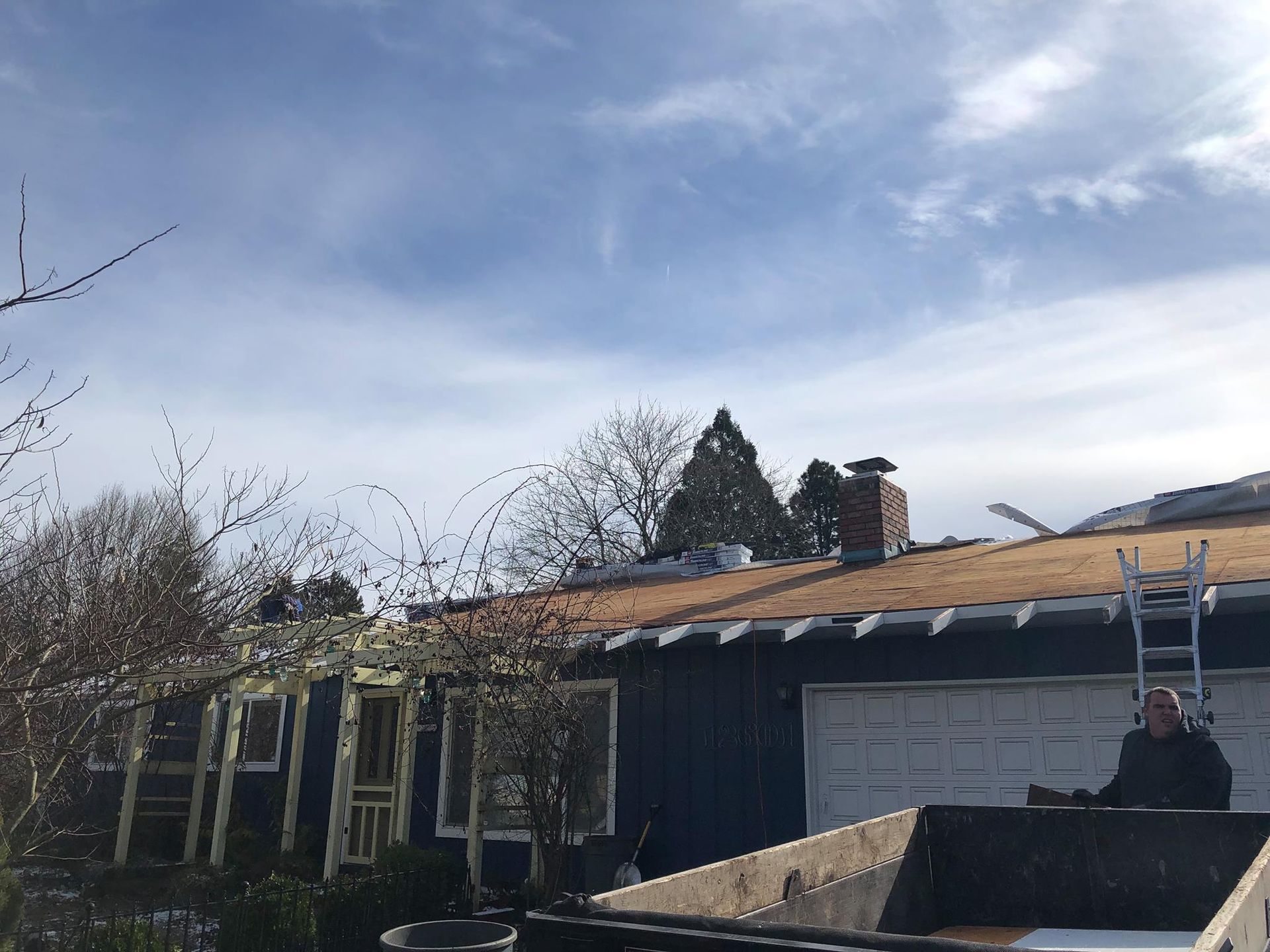 A dumpster is sitting in front of a house with a ladder on the back of it.