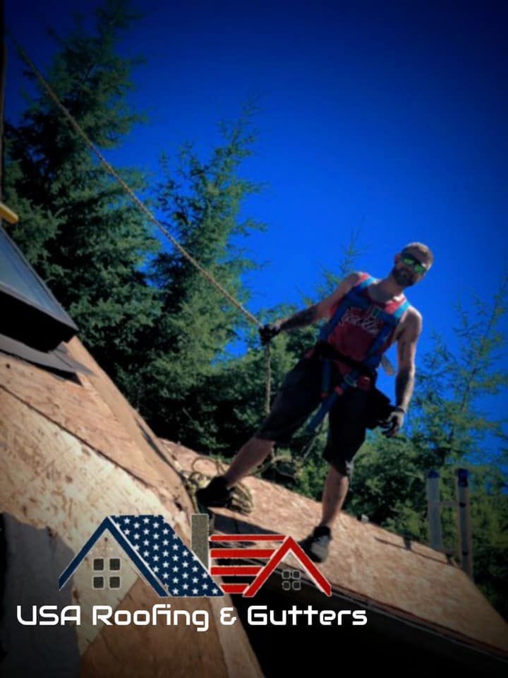 A man is standing on top of a roof with usa roofing and gutters written on the bottom