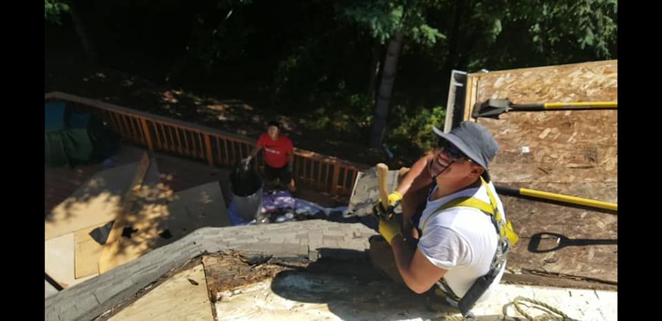 A man is kneeling down on a roof with a shovel.