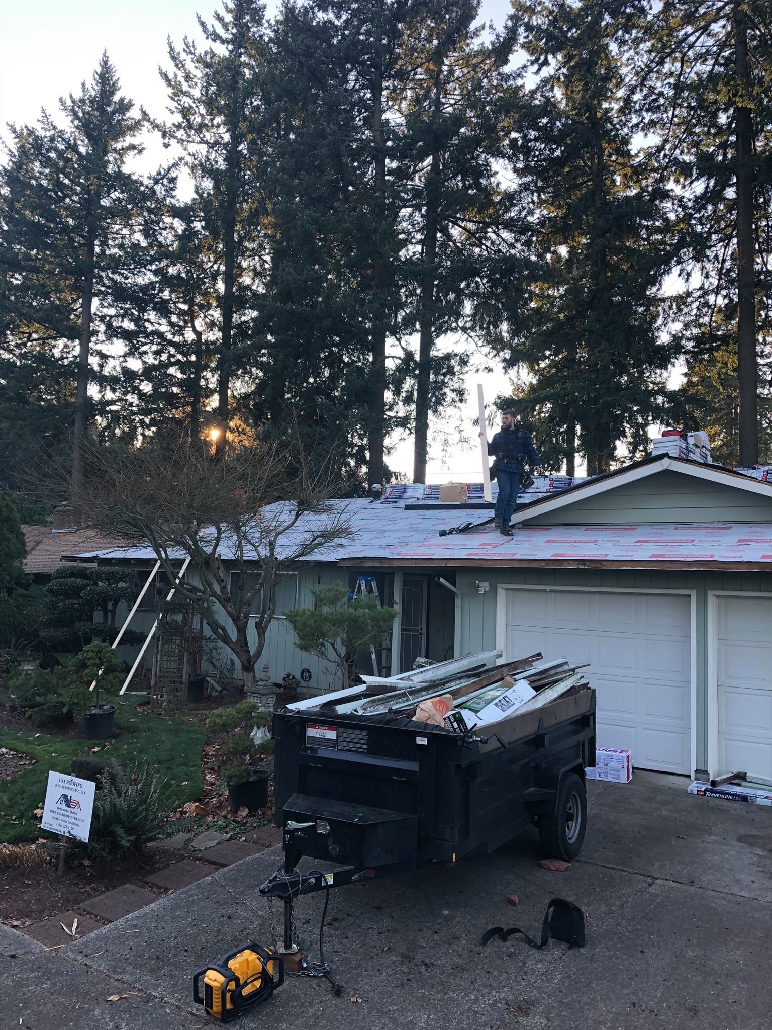 A man is working on the roof of a house next to a trailer.