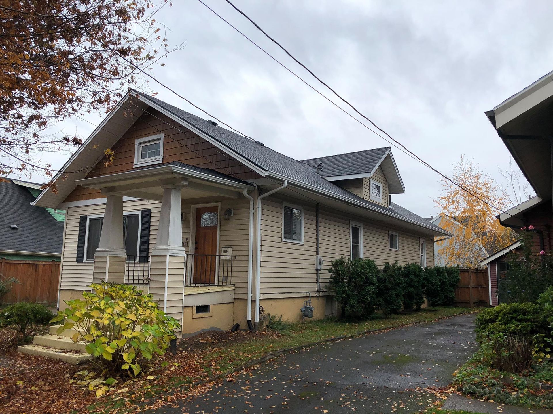 A house with a porch and a gray roof is in a residential area.