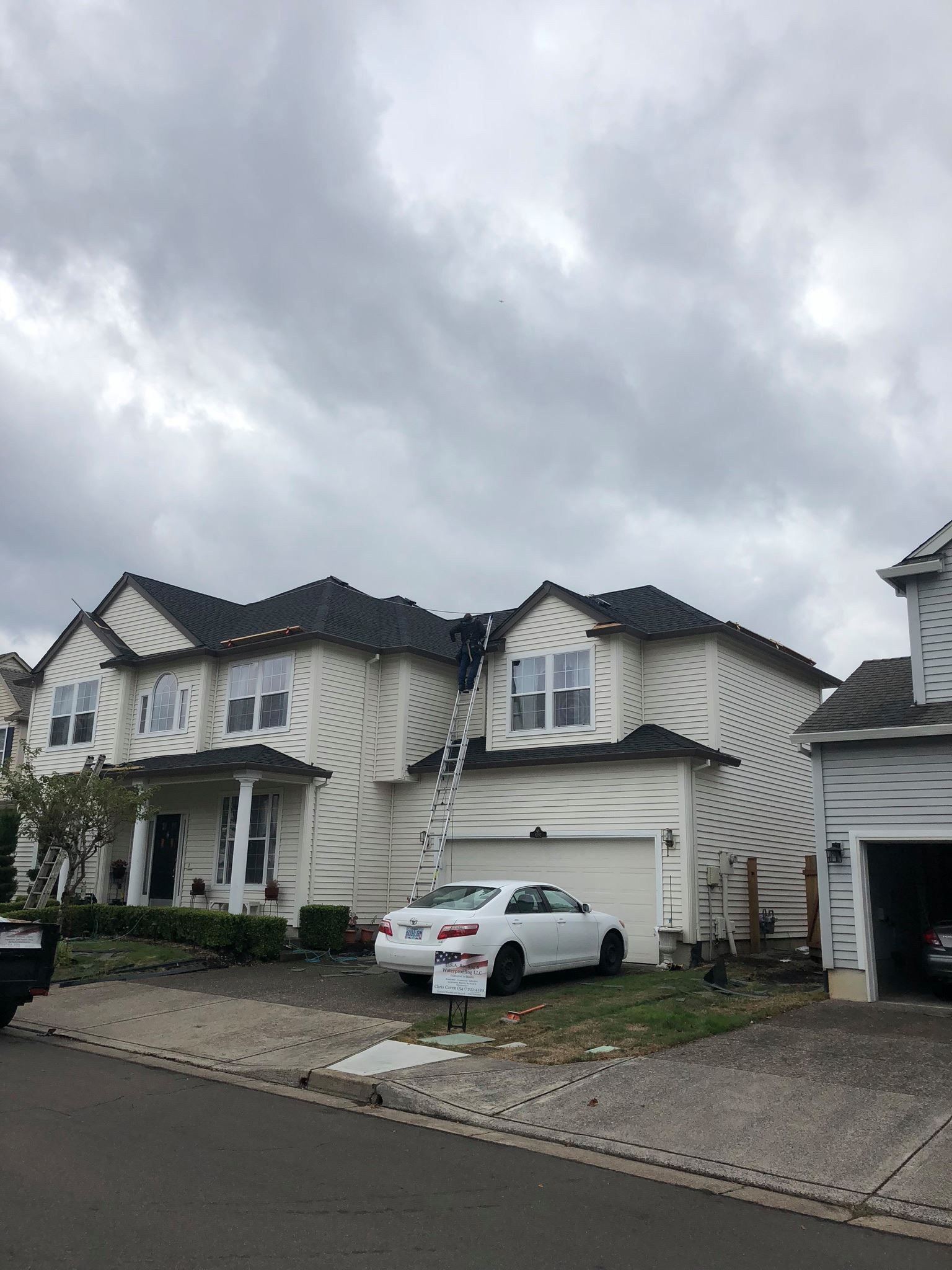 A white car is parked in front of a large white house.