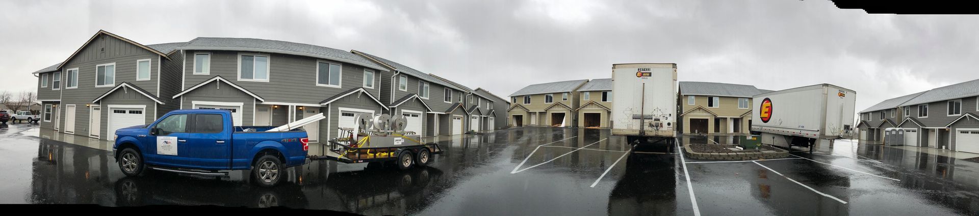 A blue truck is parked on the side of the road in front of a row of houses.