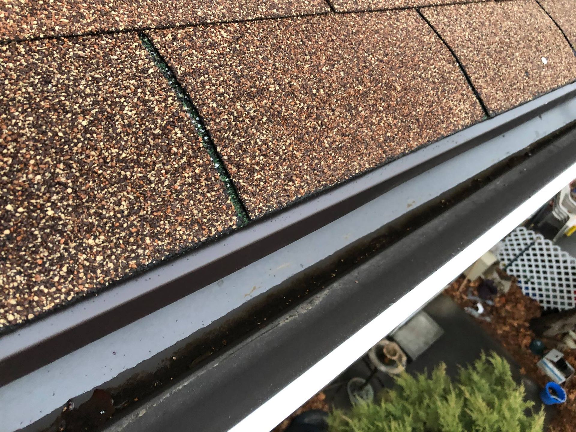 A close up of a gutter on a roof with shingles.