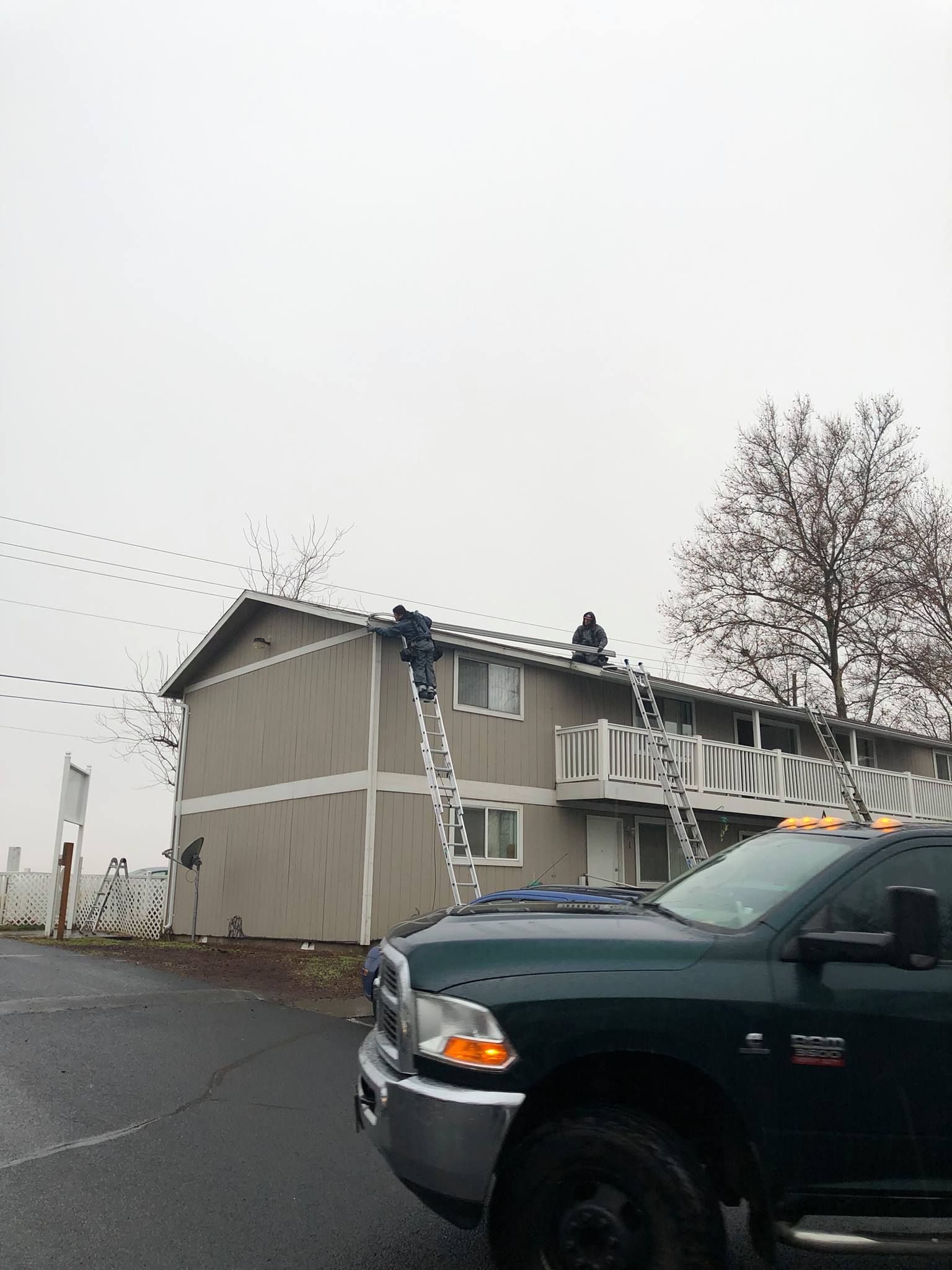 A truck is parked in front of a building with a man on the roof.