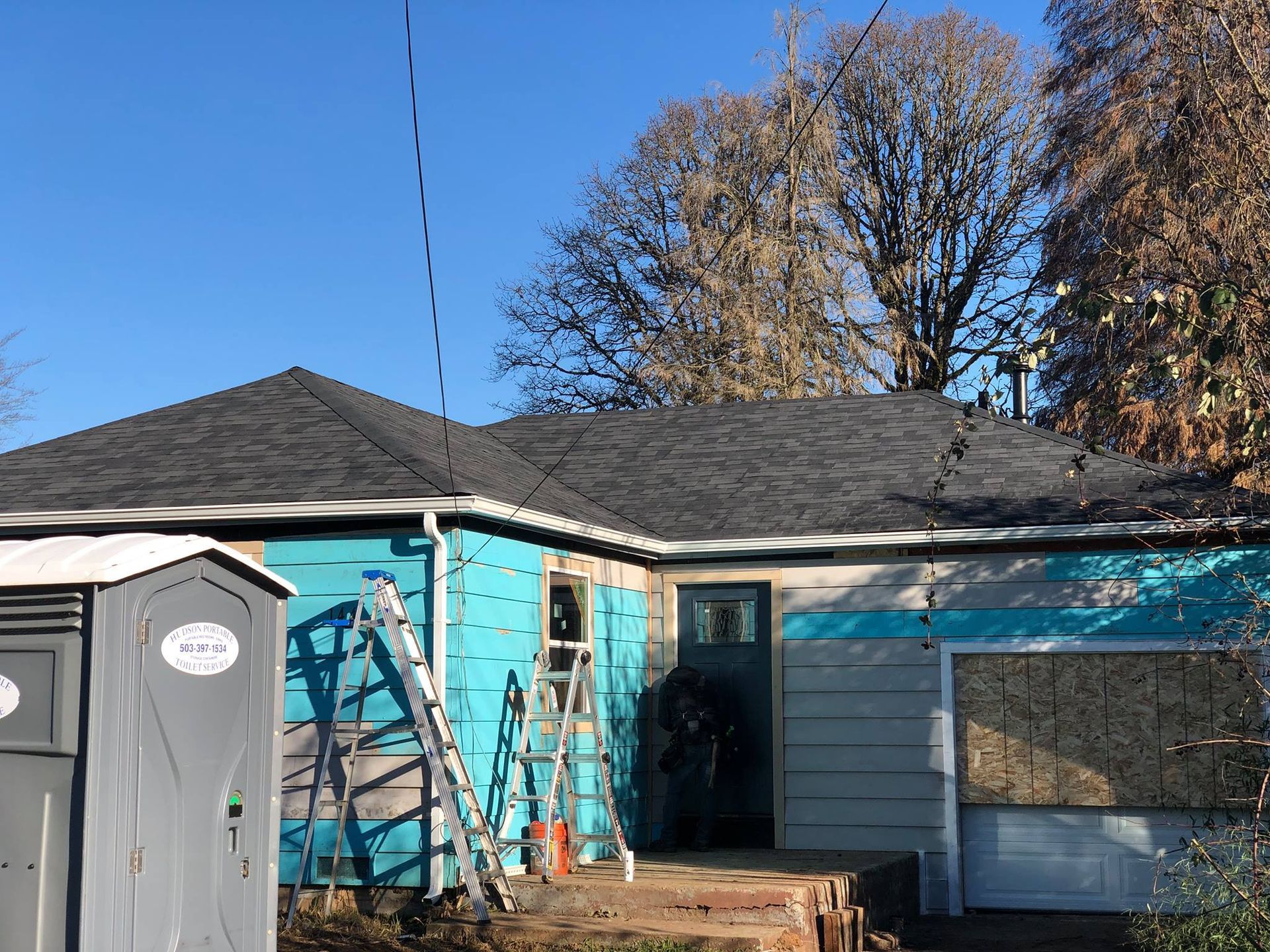 A house with a ladder and a portable toilet in front of it.