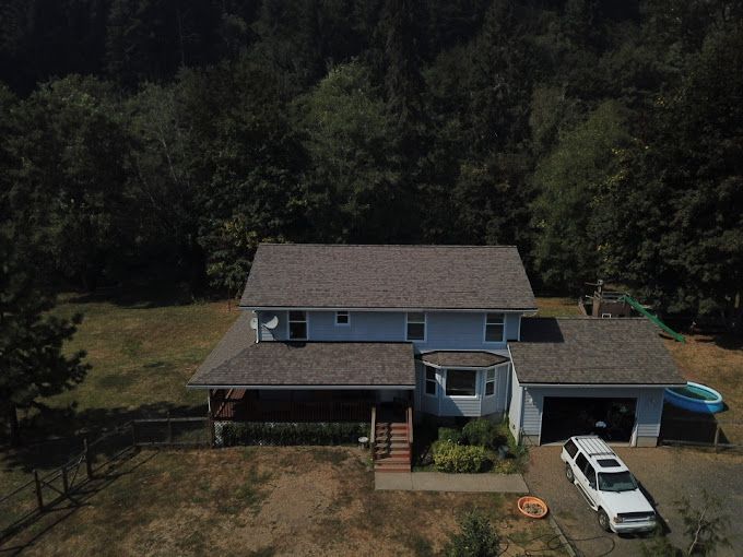 An aerial view of a house with a car parked in front of it surrounded by trees.