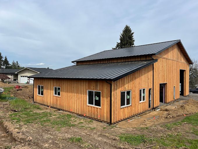 A large wooden building with a black roof is sitting in the middle of a field.