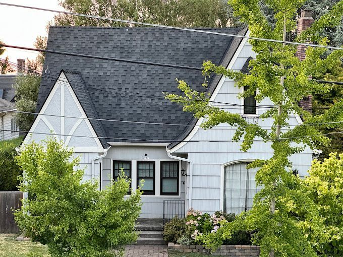 A white house with a black roof is surrounded by trees and power lines.