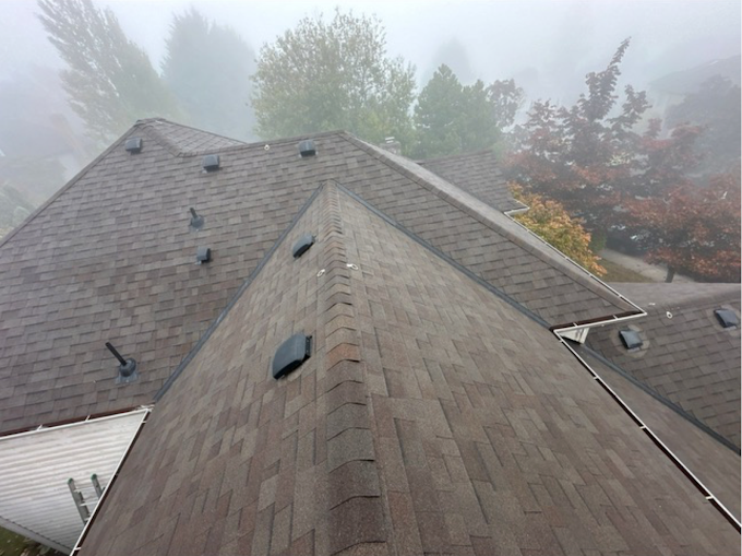The roof of a house is covered in shingles on a foggy day.