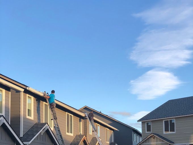A man is standing on a ladder on the roof of a house.