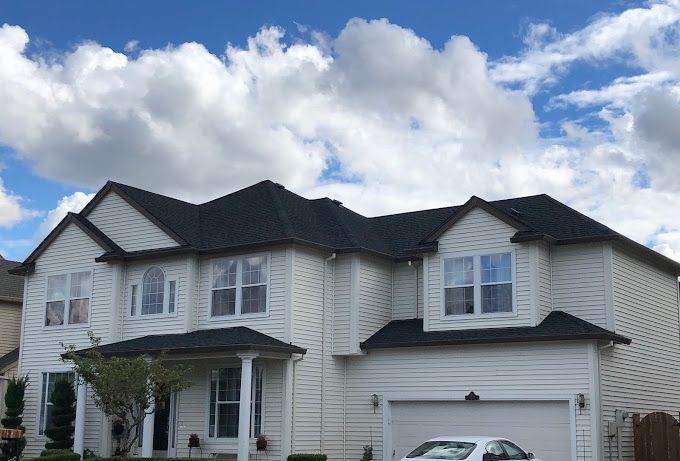 A white house with a black roof and a car parked in front of it.