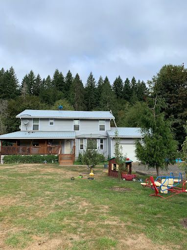 A large white house with a metal roof is surrounded by trees.