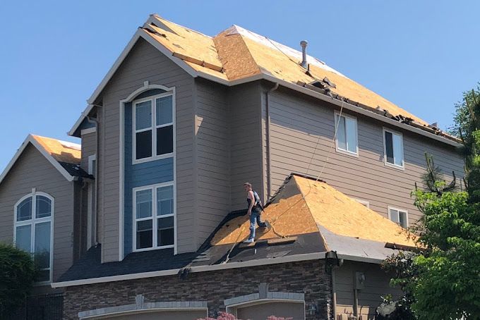 A man is standing on the roof of a large house.
