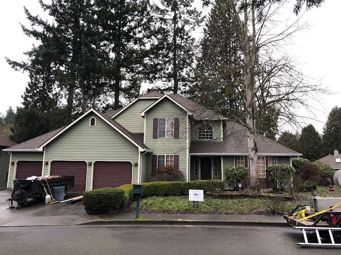 A green house with a brown garage door is surrounded by trees.