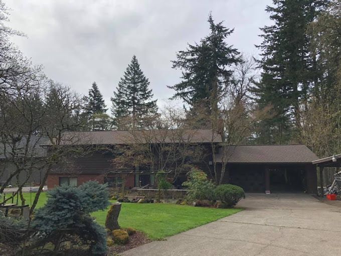 A large house with a driveway and trees in the background.