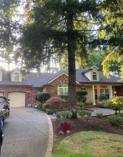 A car is parked in front of a brick house surrounded by trees.