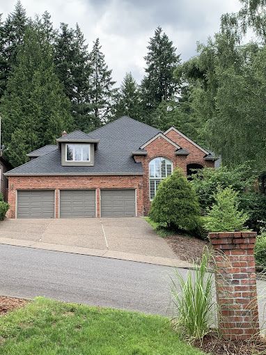 A large brick house with three garage doors is surrounded by trees.